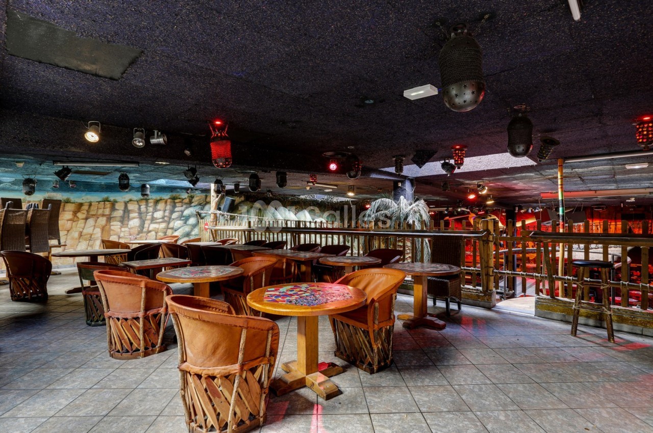 Salle de restaurant avec tables en bois, chaises en cuir et décoration intérieure évoquant un style tropical.