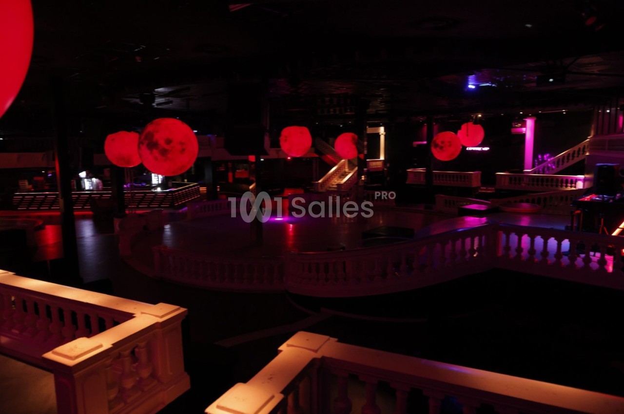 Salle de discothèque sombre avec éclairage rouge, piste de danse centrale et balustrades blanches.