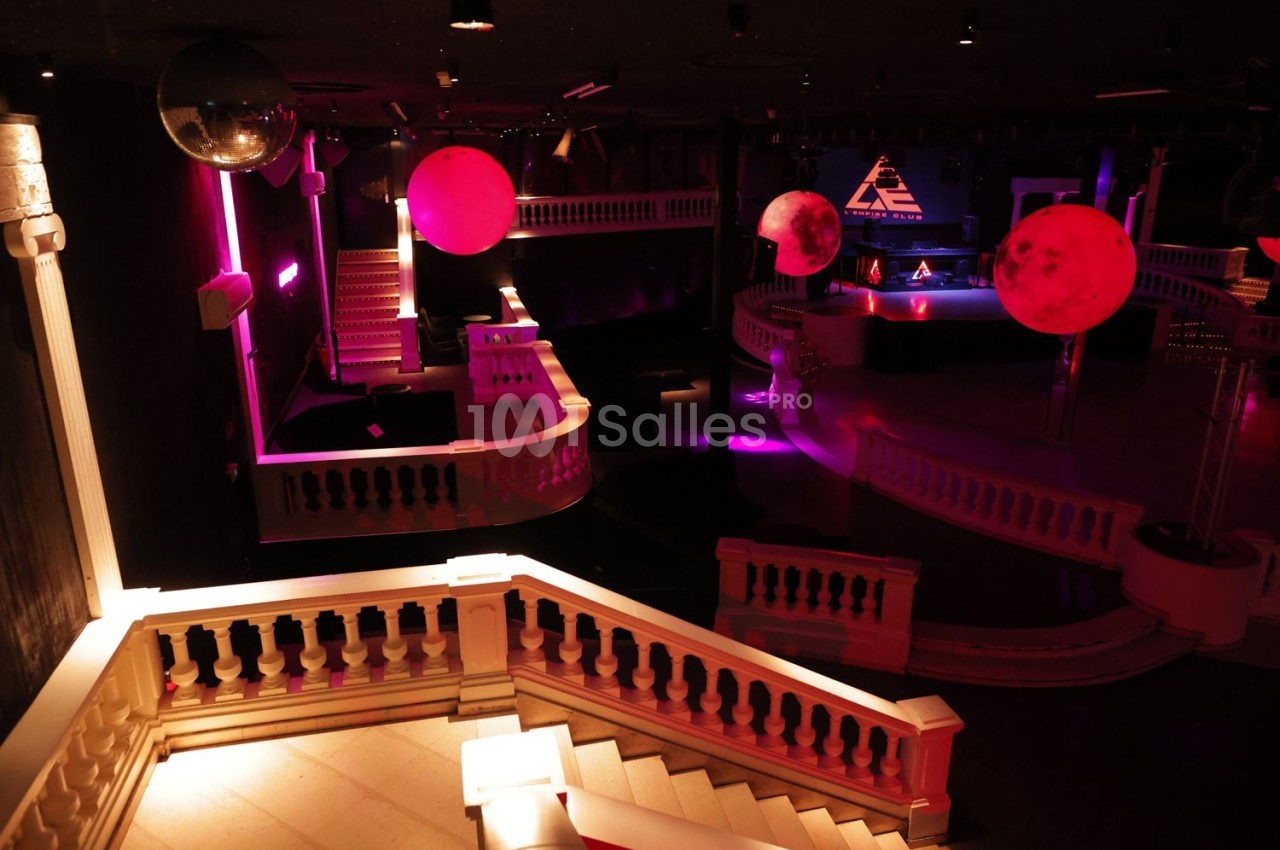 Intérieur d'une discothèque avec éclairage tamisé, boules lumineuses rouges et balustrades blanches.