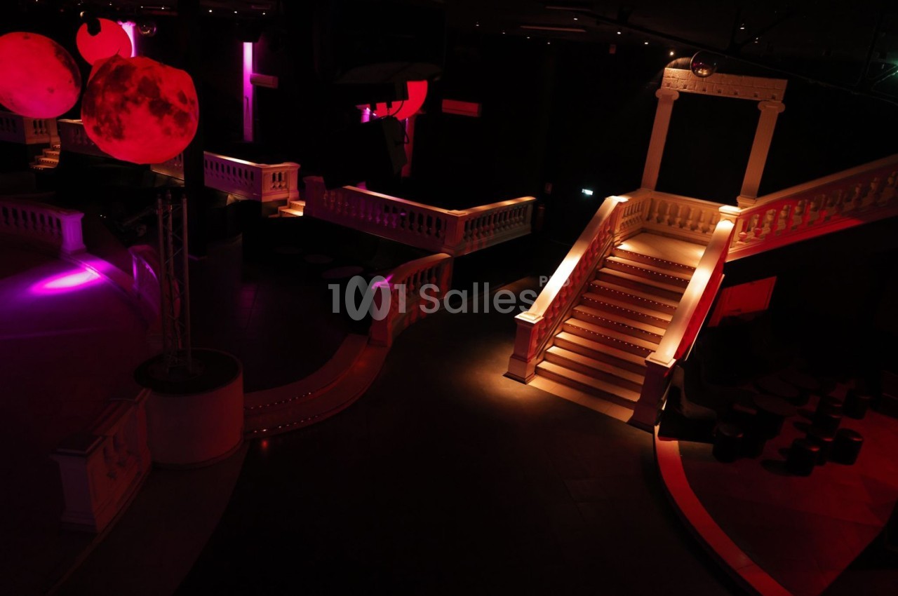 Escalier éclairé dans une salle sombre avec des lumières colorées et des décorations suspendues.