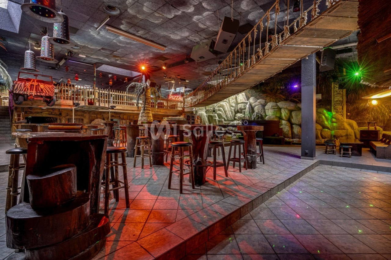 Salle de bar à thème avec pont suspendu, tables en bois et éclairage coloré dans une ambiance tropicale.