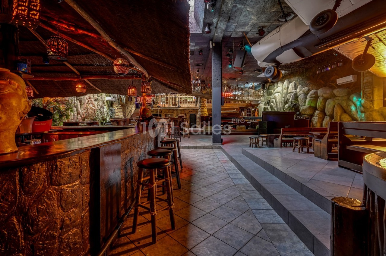 Intérieur d'un bar à thème avec comptoir en bois, tabourets, éclairage tamisé et décorations exotiques.