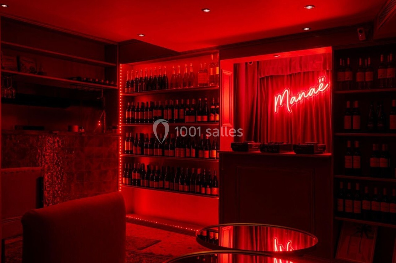 Salle tamisée avec éclairage rouge, étagères remplies de bouteilles de vin et enseigne lumineuse ’Marie’ au mur.