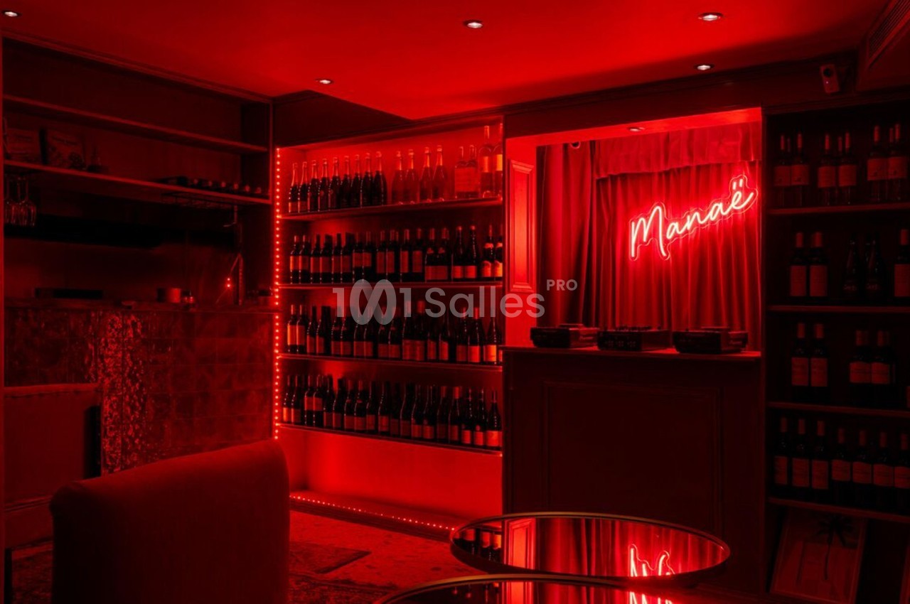 Salle tamisée avec éclairage rouge, étagères remplies de bouteilles de vin et enseigne lumineuse ’Marie’ au mur.