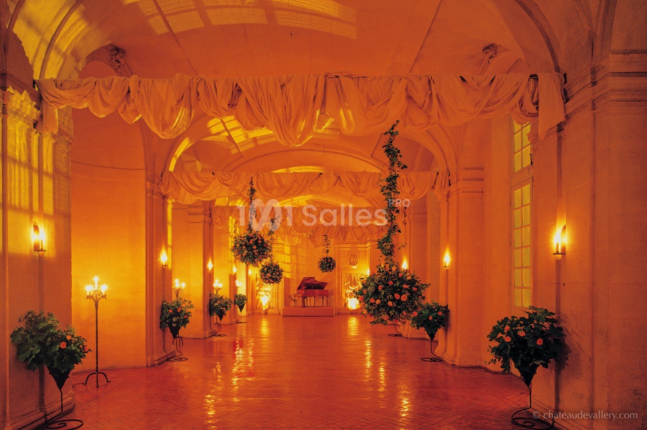 Salle voûtée illuminée par des chandeliers, décorée de drapés suspendus et de plantes fleuries.