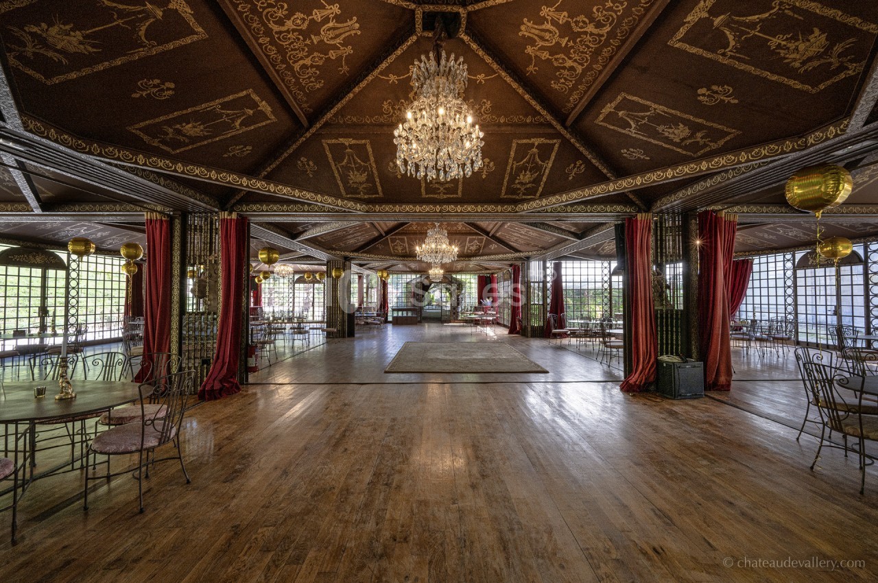 Salle de réception spacieuse avec parquet en bois, lustres, plafonds ornés et grandes baies vitrées entourées de rideaux…