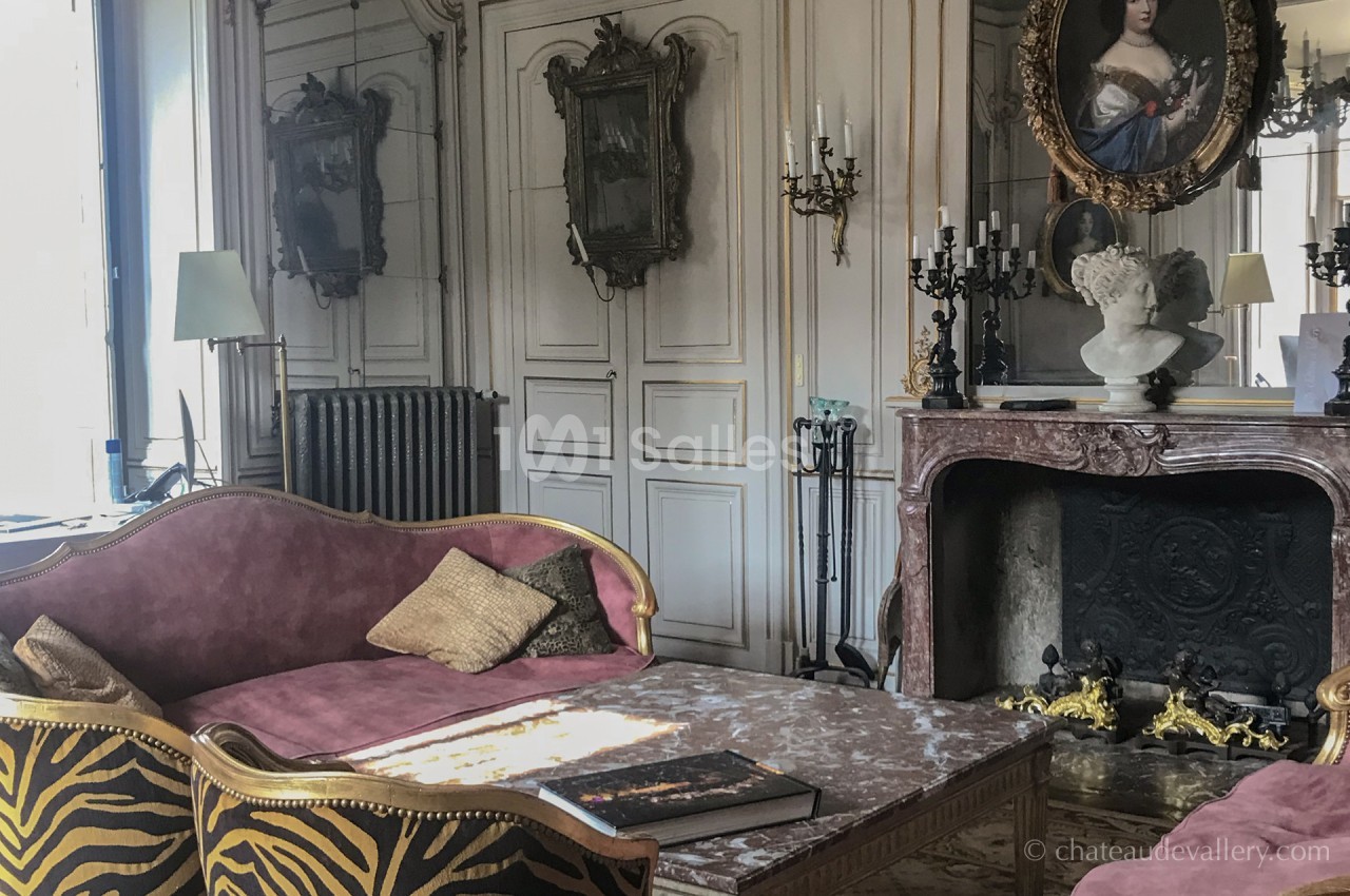 Salon élégant avec canapé en velours, cheminée ornée, miroir ancien et décoration classique.