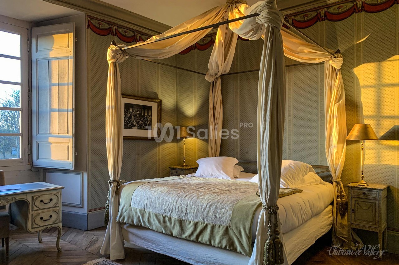 Lit à baldaquin dans une chambre élégante avec lumière naturelle, murs texturés et mobilier classique.