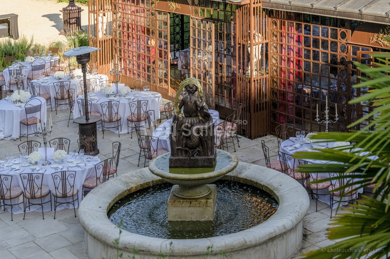 Fontaine centrale entourée de tables dressées pour un événement en extérieur, avec une façade vitrée en arrière-plan.