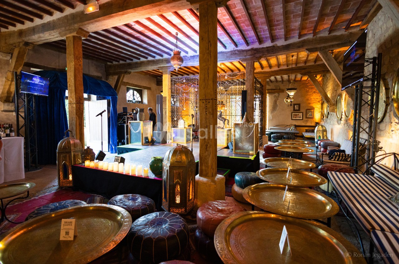 Salle décorée dans un style oriental avec des tables basses dorées, des poufs colorés et une scène éclairée.