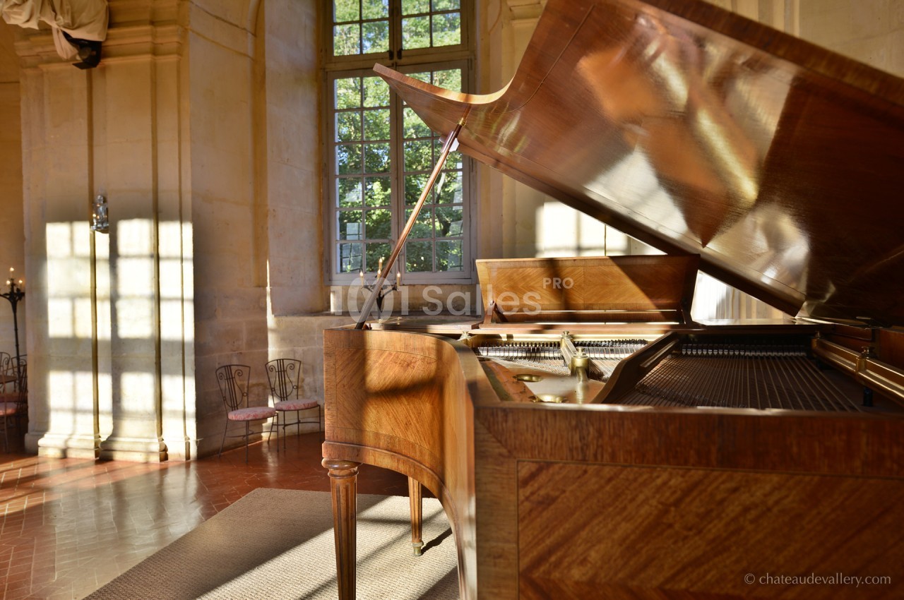 Piano à queue en bois dans une pièce lumineuse avec de grandes fenêtres et des murs en pierre.