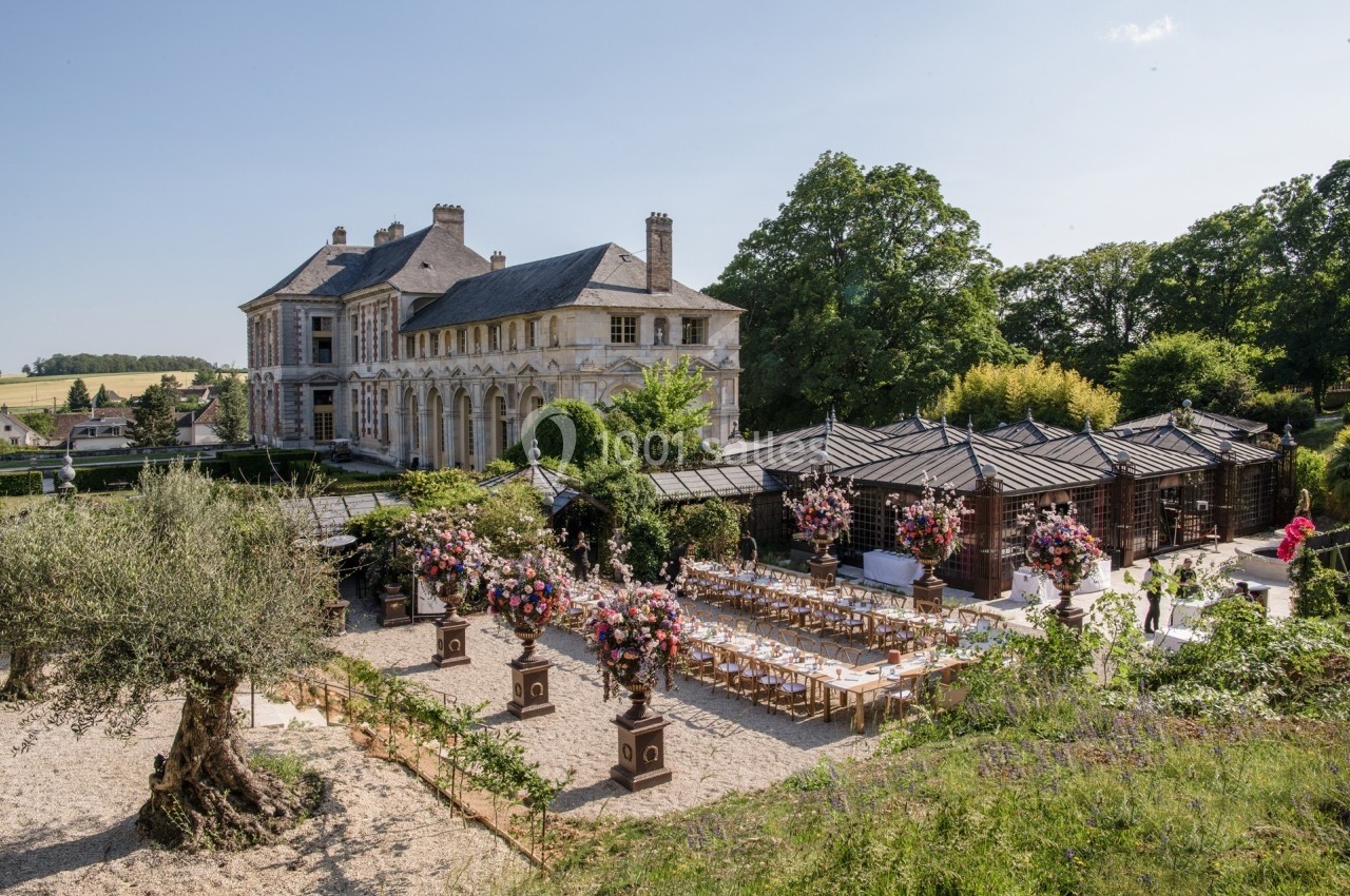 Tables dressées pour un événement en plein air devant un château entouré de jardins et de verdure.