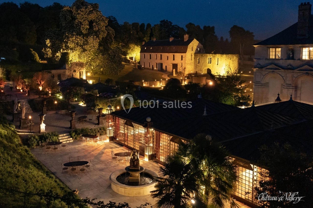 Vue nocturne d'un domaine avec bâtiments historiques éclairés, jardin aménagé et fontaine centrale.