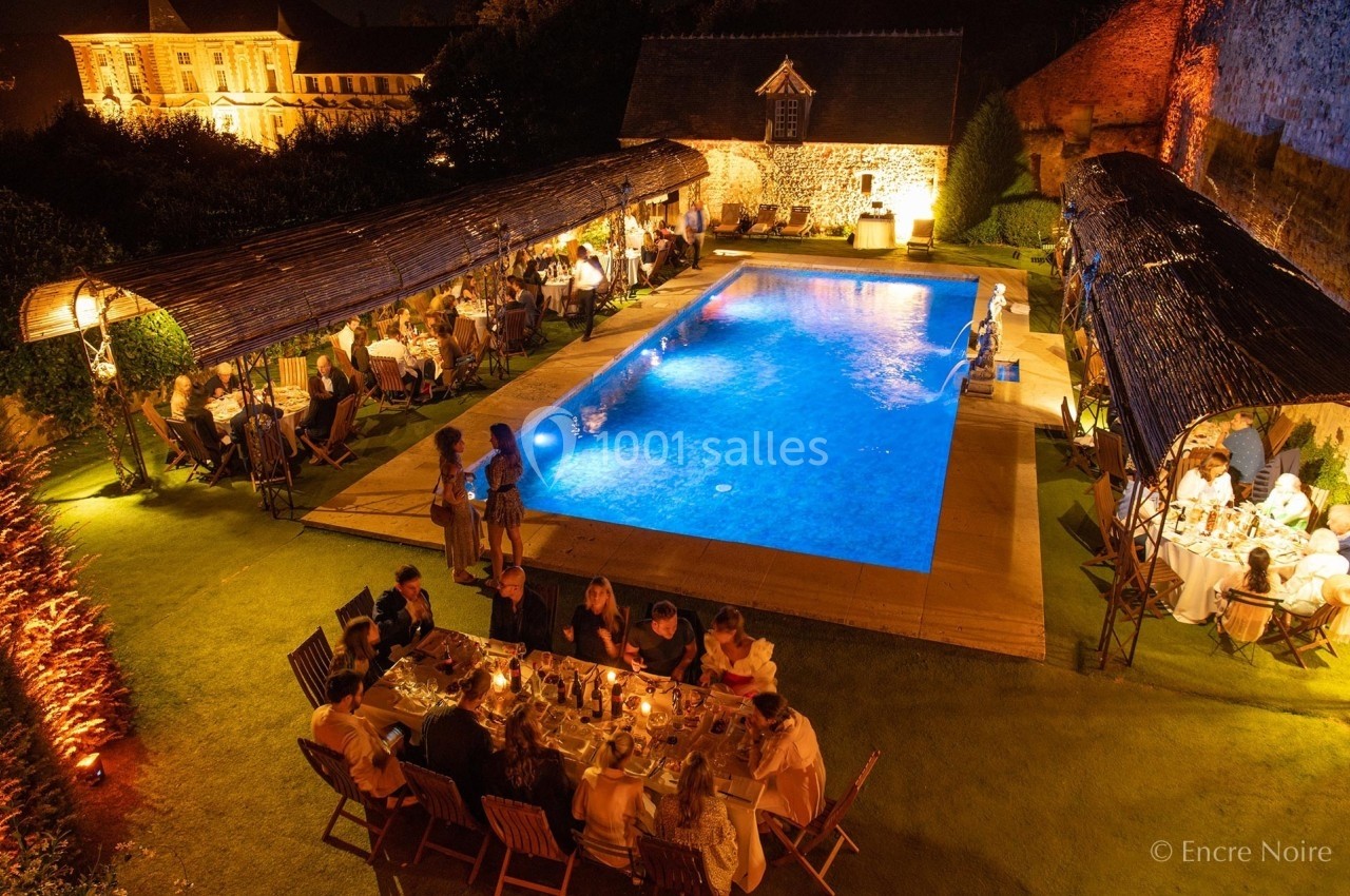 Dîner en plein air autour d'une piscine éclairée, avec des convives assis sous des pergolas et à une table centrale.