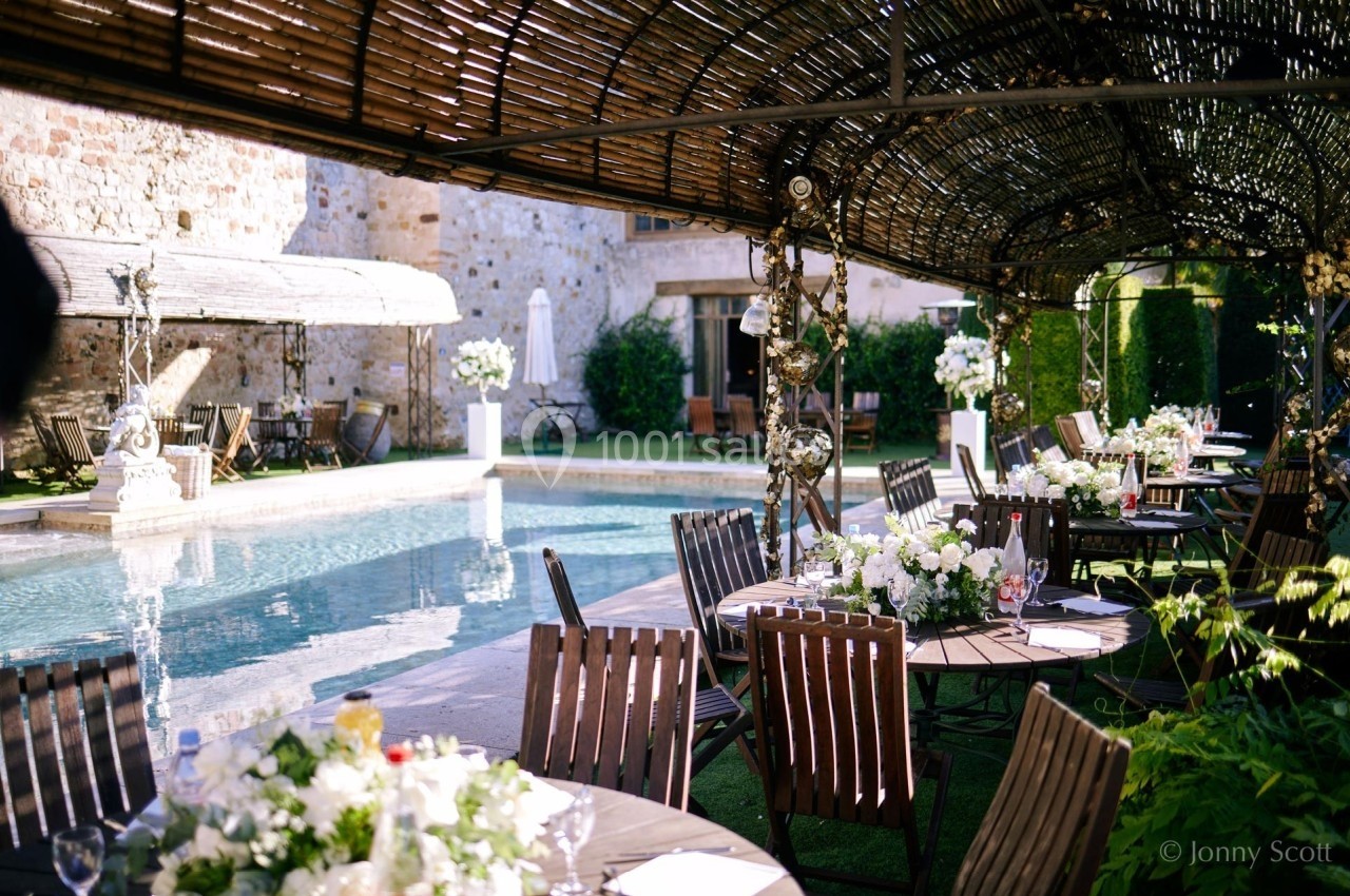 Tables décorées avec des fleurs blanches disposées près d'une piscine, sous une pergola en bois, dans un cadre élégant.
