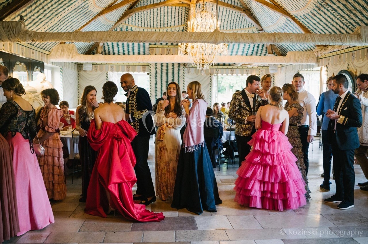 Personnes en tenue de soirée discutant dans une salle élégante avec un plafond en bois et un lustre.