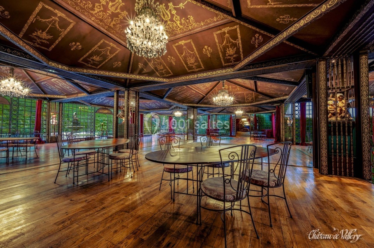 Salle spacieuse avec parquet en bois, tables et chaises en fer forgé, lustres suspendus et décorations murales élégantes.