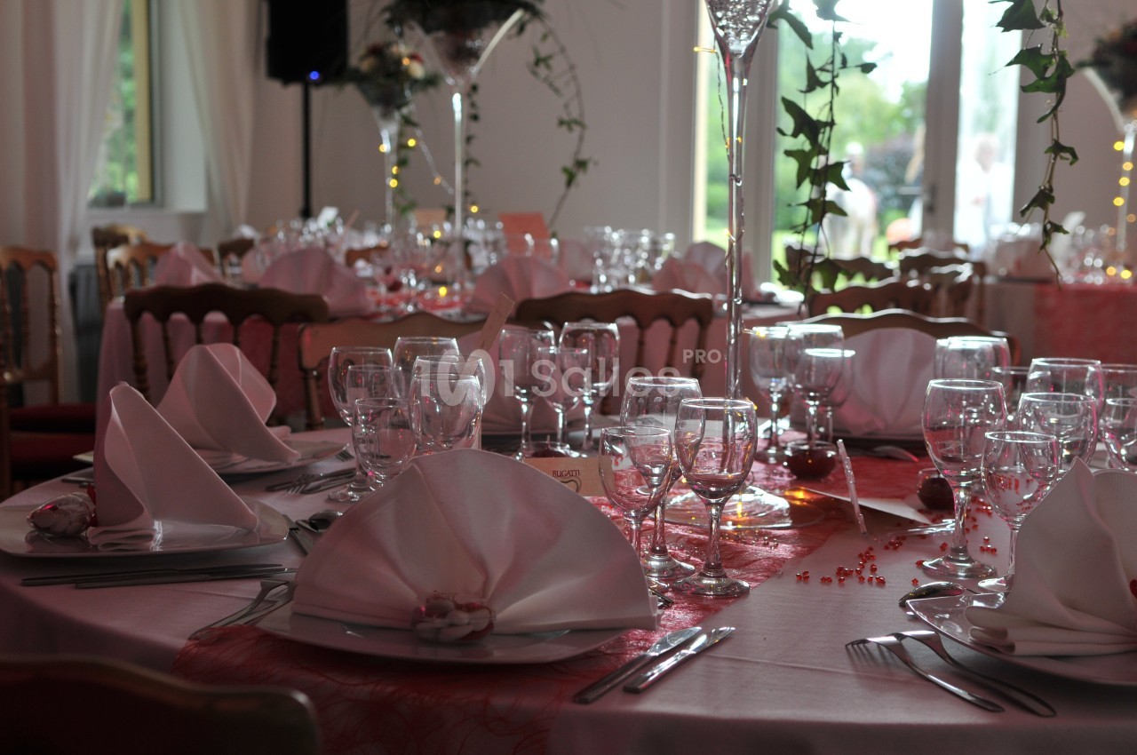 Table élégamment dressée avec nappes blanches, serviettes pliées, verres et couverts dans une salle lumineuse.