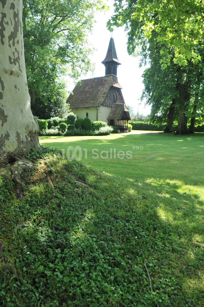 Petite chapelle en bois entourée de verdure, située dans un parc arboré et baignée par une lumière naturelle.