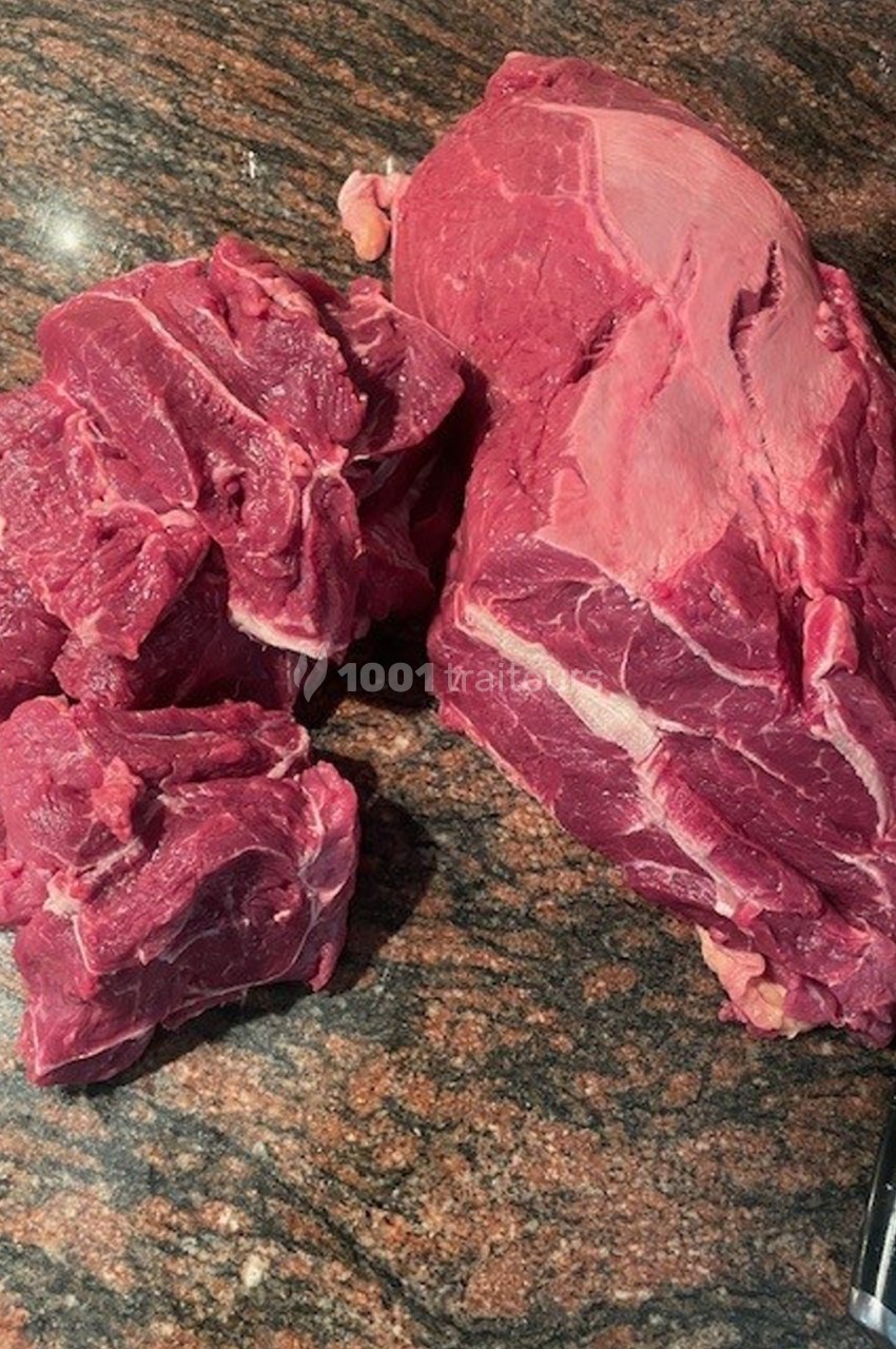 Morceaux de viande rouge crue posés sur un plan de travail en pierre brune.