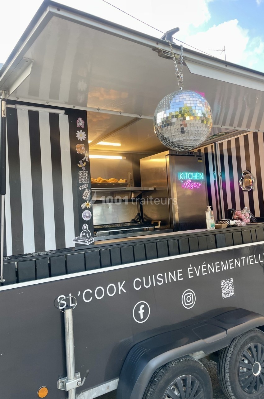 Food truck noir avec décoration rayée, boule disco suspendue et enseigne lumineuse ’Kitchen Disco’ à l'intérieur.
