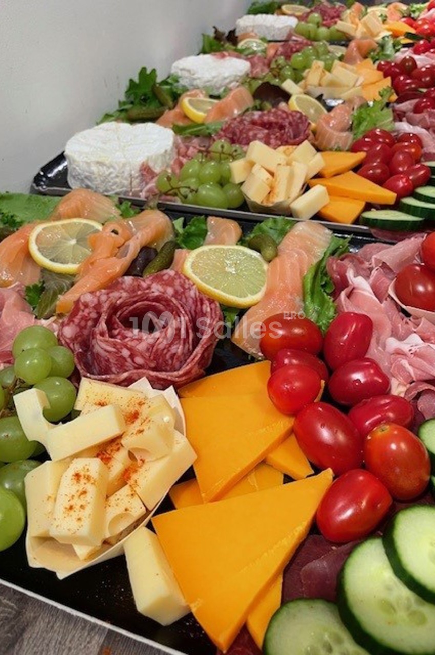 Plateau coloré composé de fromages, charcuteries, saumon fumé, légumes frais et fruits disposés harmonieusement.