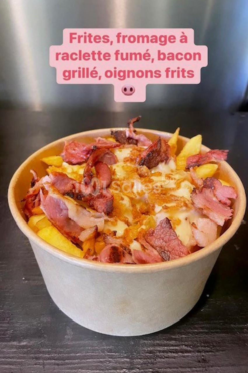Bol de frites garnies de fromage à raclette fumé, bacon grillé et oignons frits, posé sur une surface sombre.