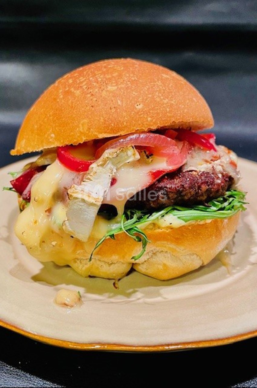 Burger garni de fromage fondu, légumes frais et oignons rouges, présenté sur une assiette beige.