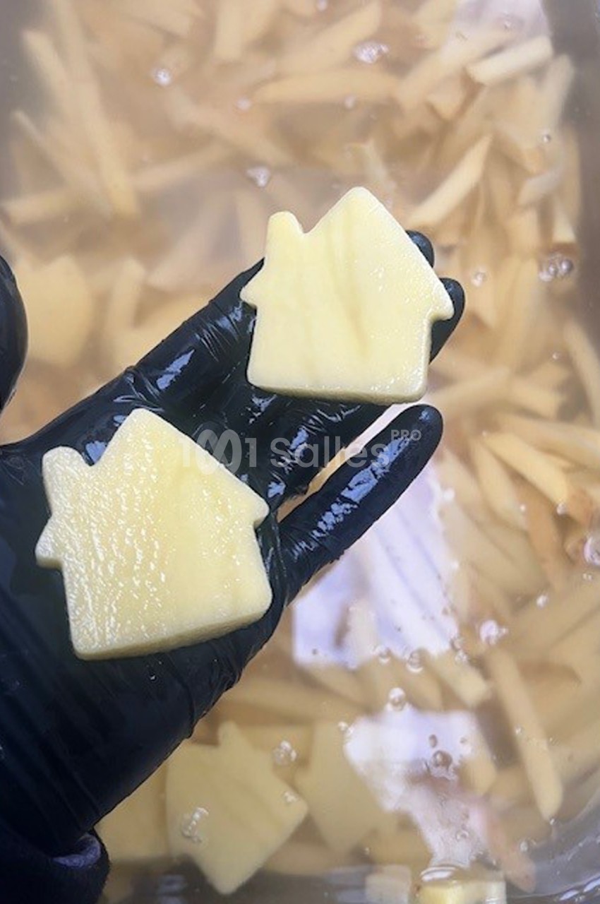 Deux morceaux de pommes de terre découpés en forme de maison, tenus par une main gantée au-dessus d'eau.
