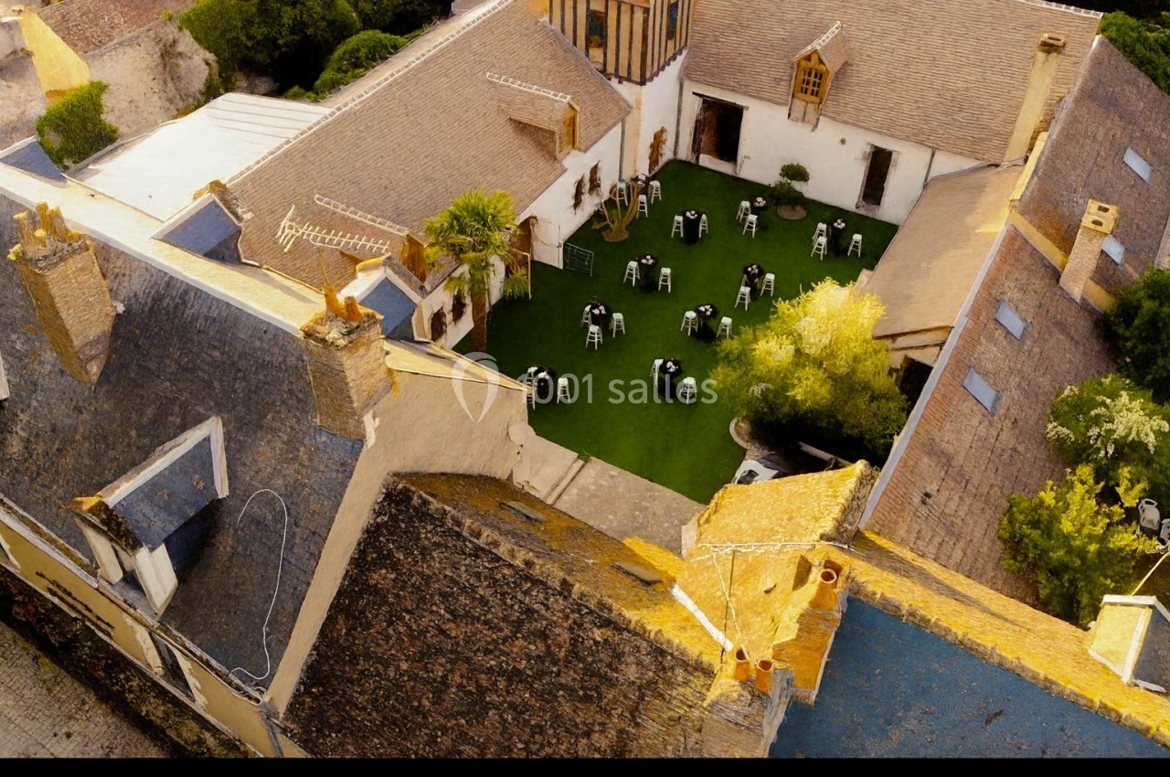 Vue aérienne d'une cour intérieure avec pelouse, tables rondes dressées et bâtiments anciens autour.