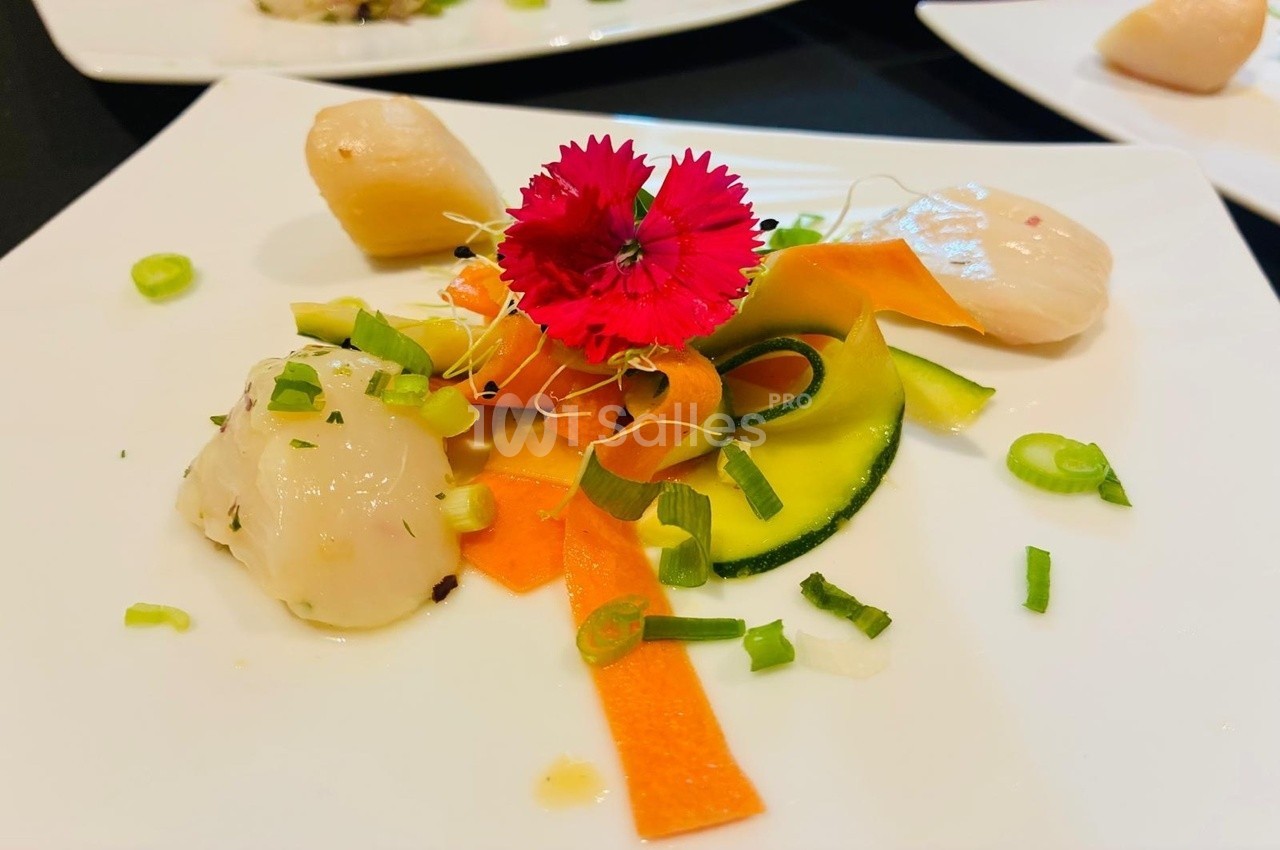 Assiette de carpaccio de Saint-Jacques avec légumes colorés, fleurs comestibles et ciboulette hachée.
