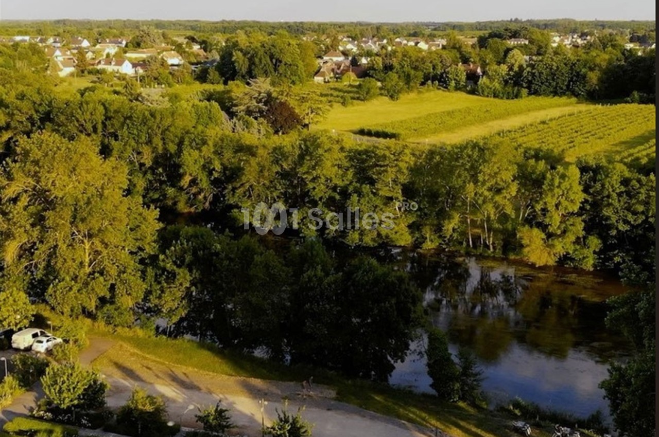 Vue aérienne d'une campagne verdoyante avec des champs, des arbres, une rivière et des habitations au loin.
