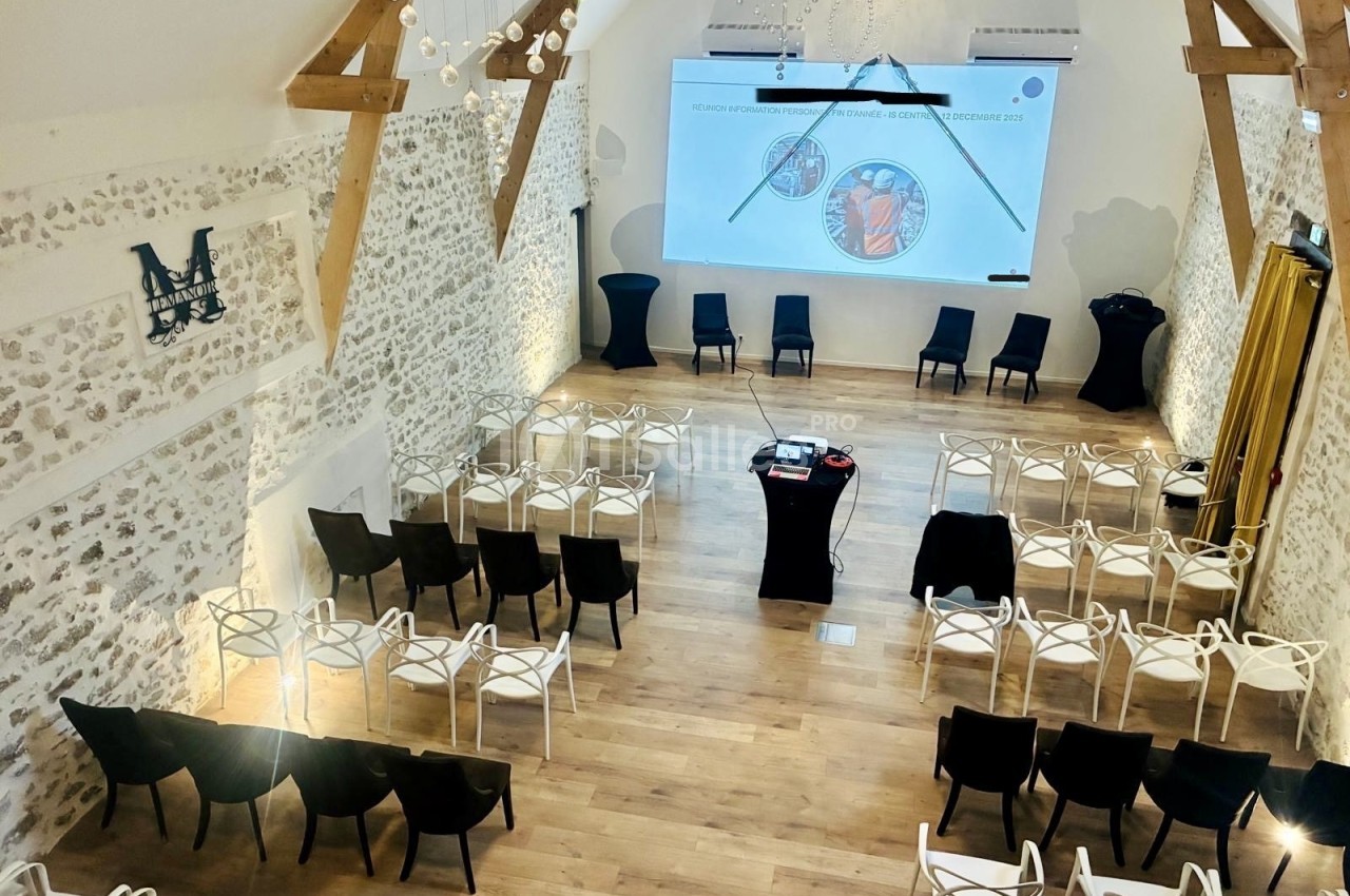 Salle de conférence lumineuse avec des chaises disposées face à un écran de projection dans un espace au décor rustique.