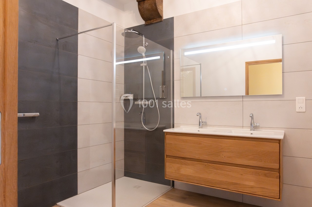 Salle de bain moderne avec douche à l'italienne, meuble double vasque en bois et grand miroir éclairé.