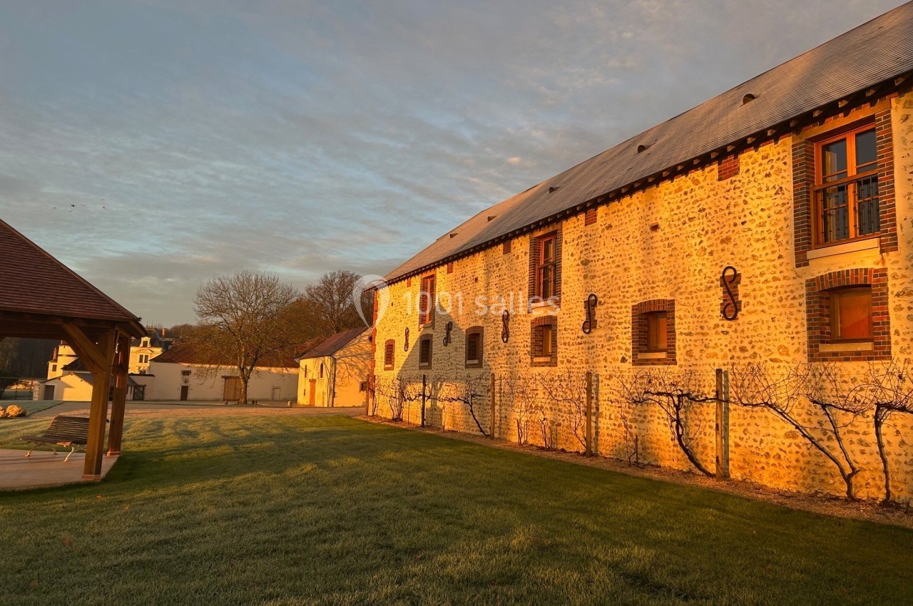 Bâtiment en pierre éclairé par le soleil couchant, avec une pelouse au premier plan et un ciel partiellement nuageux.