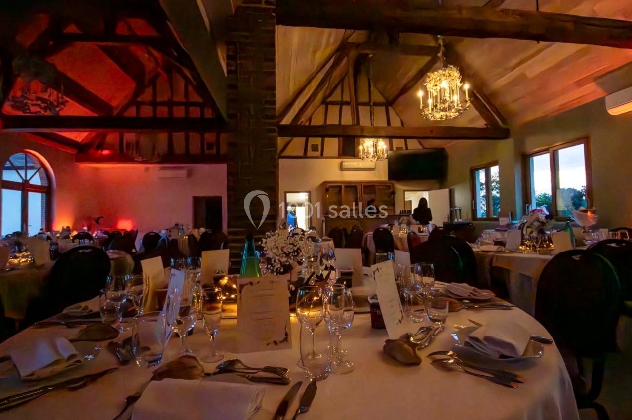 Salle de réception avec tables dressées, décorations élégantes, poutres apparentes et éclairage chaleureux.