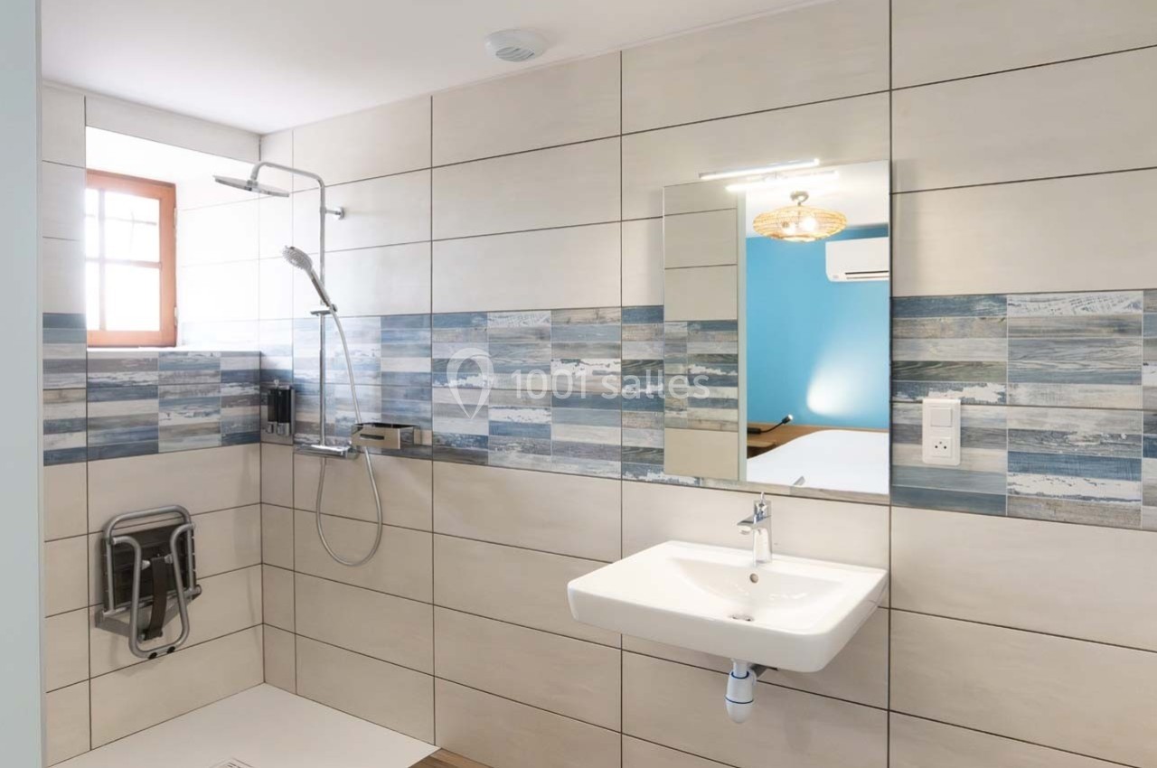 Salle de bain moderne avec douche à l'italienne, lavabo suspendu et carrelage beige et bleu.