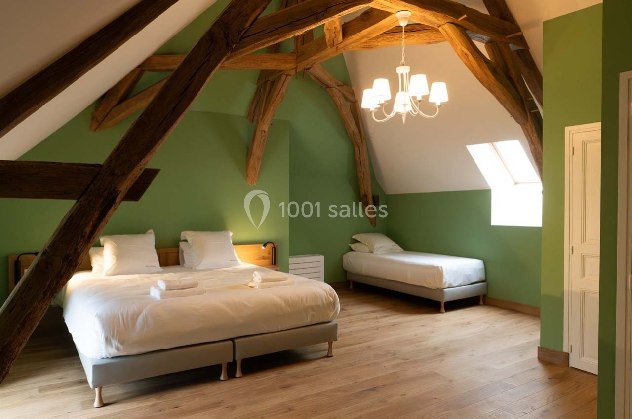 Chambre mansardée avec poutres apparentes, murs verts, lit double, lit simple, parquet et lumière naturelle.