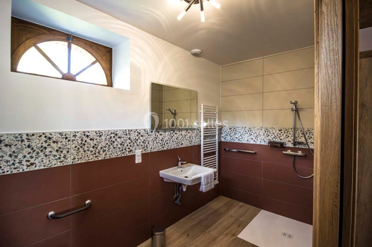 Salle de bain accessible avec douche à l'italienne, lavabo mural, barre d'appui et fenêtre en arche.