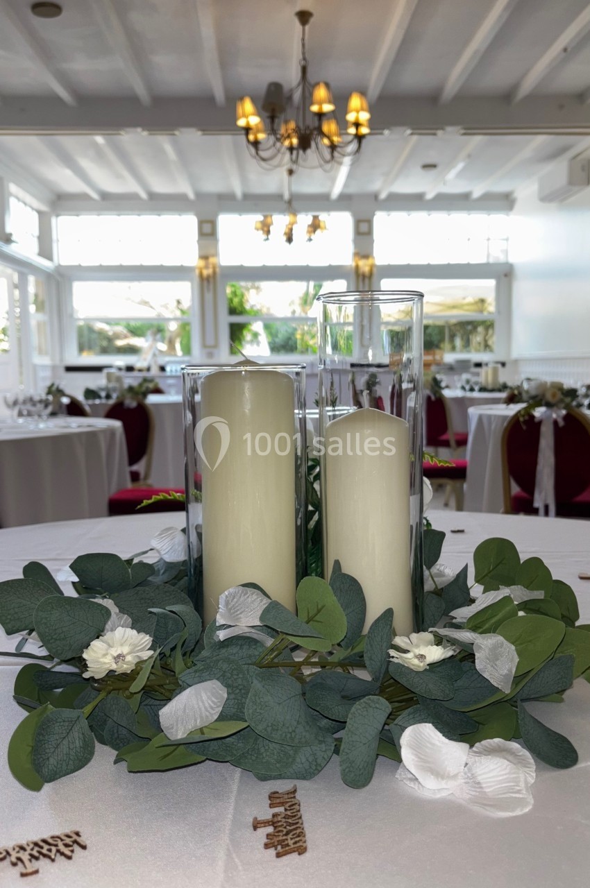 Centre de table avec bougies blanches dans des cylindres en verre, entourées de feuillage et de fleurs blanches.