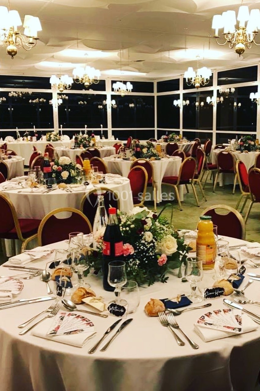 Salle de réception élégamment décorée avec des tables rondes dressées, ornées de fleurs et de vaisselle raffinée.