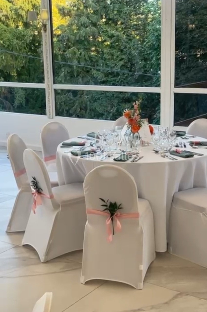 Table ronde dressée pour un événement, avec nappes blanches, chaises décorées et un centre de table floral.