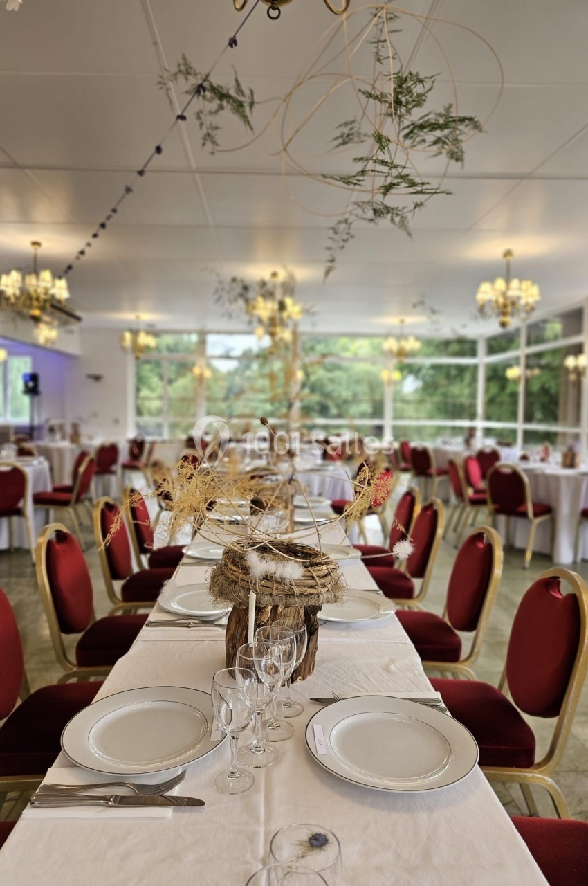 Salle de réception décorée avec des tables dressées, chaises rouges et ornements végétaux suspendus.