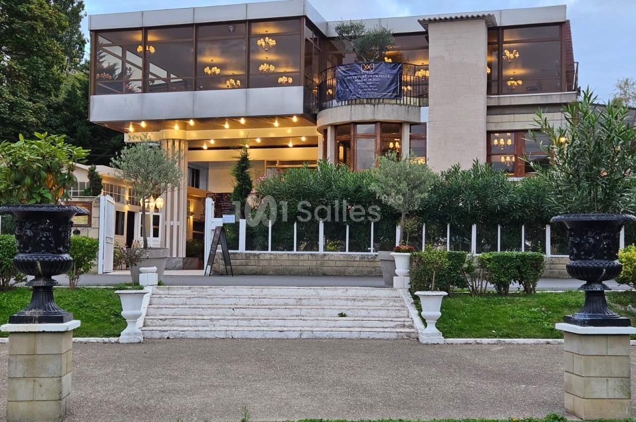 Façade d'un restaurant moderne avec grandes baies vitrées, terrasse éclairée et jardin aménagé à l'avant.