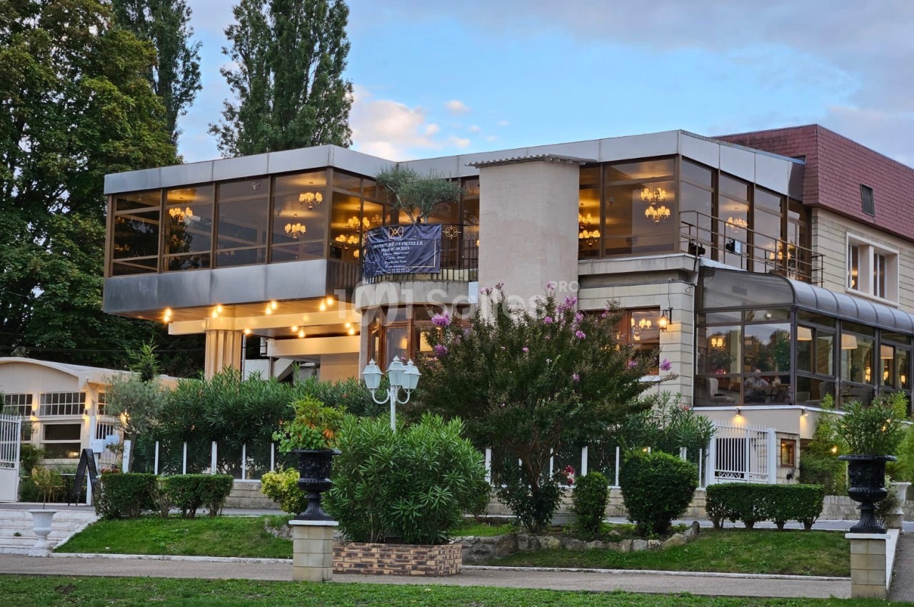 Bâtiment moderne avec grandes baies vitrées, entouré de verdure et éclairé par des lumières chaudes en soirée.