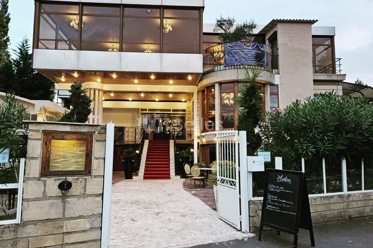 Façade d'un restaurant avec une entrée surmontée de grandes baies vitrées et un tapis rouge menant à la porte principale.