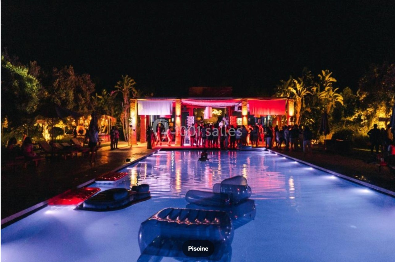 Soirée festive autour d'une piscine éclairée, avec des invités et une ambiance lumineuse colorée.