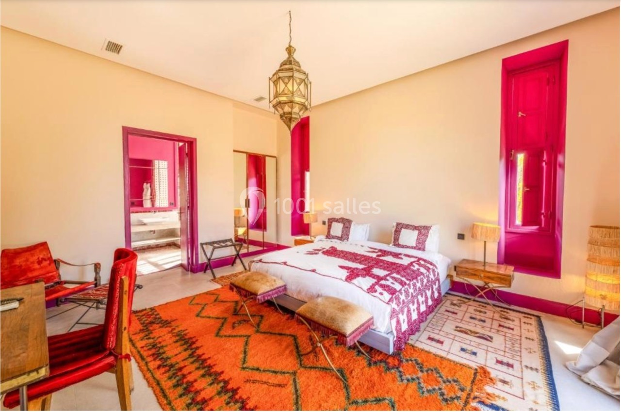Chambre lumineuse avec lit double, tapis colorés, murs beige et accents roses, décorée dans un style oriental.