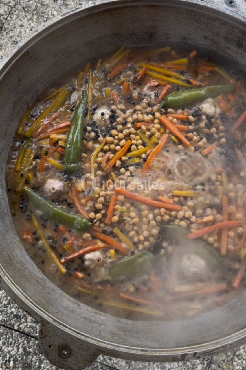 Cuisson d'un mélange de légumes, pois chiches, piments verts et épices dans une grande marmite en métal.
