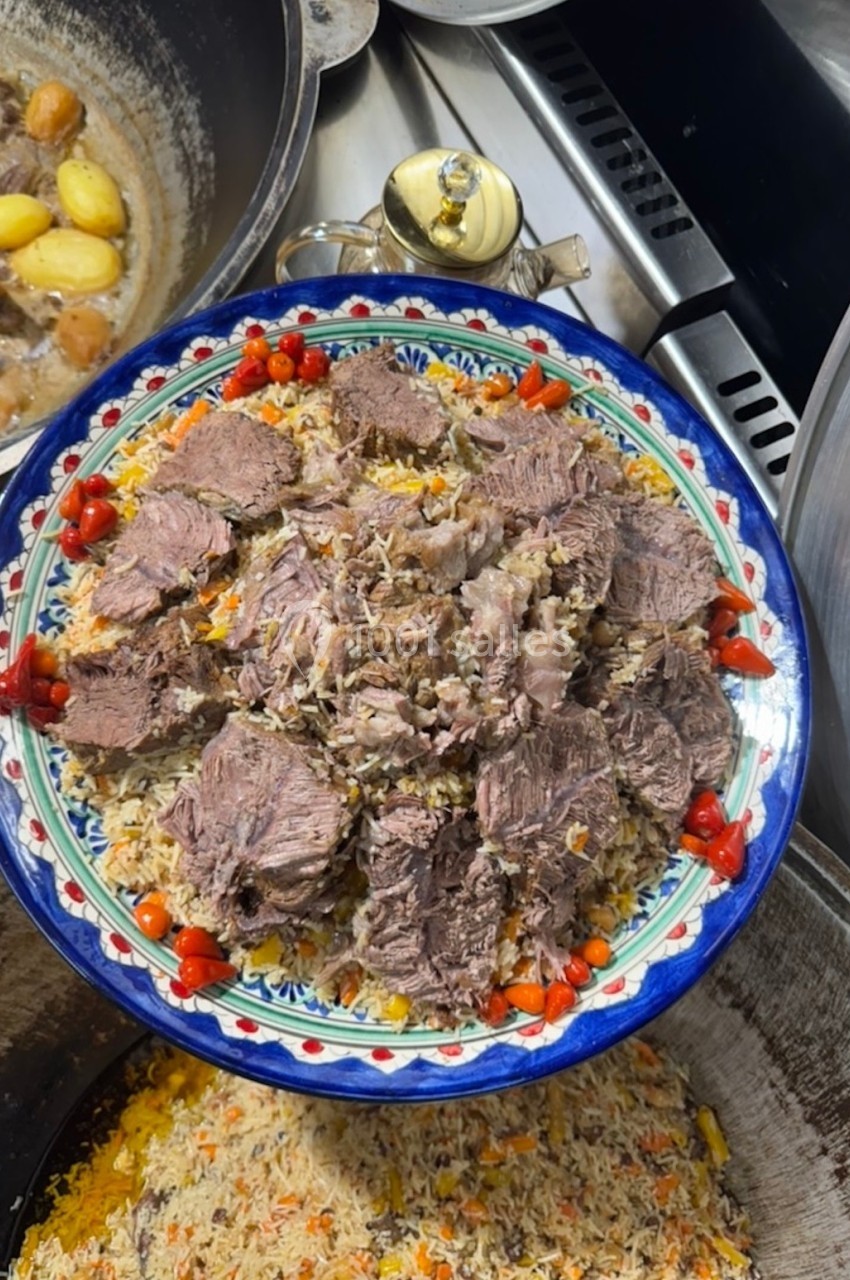 Plat de riz garni de morceaux de viande cuite, décoré de petits légumes rouges, présenté dans un grand plat coloré.